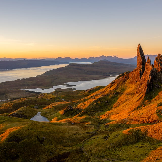Landschaftsaufnahme bei Sonnenaufgang von der Felsformation Old Man of Storr auf der Isle of Skye in Schottland, mit Blick auf das Meer und ferne Berge.