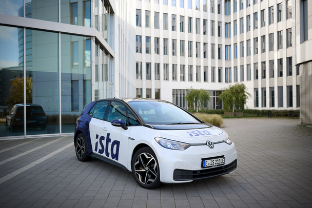 Ein weiß-blauer VW ID.3 mit ista-Logo steht vor einem modernen Bürogebäude mit Glasfassade.