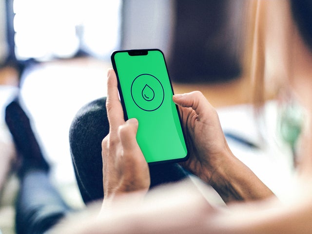 The picture shows two hands holding a smartphone into the camera frame. On the smartphone is the screen for ista’s Leakage-detection app. The rest of the picture is blurred, but the person who’s holding the phone can be seen to be sitting on the couch at home.