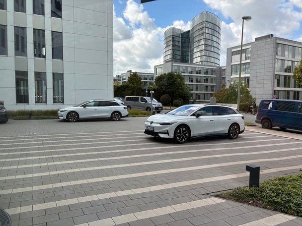 Zwei weiße Elektroautos stehen auf dem gepflasterten Vorplatz eines modernen Bürokomplexes.