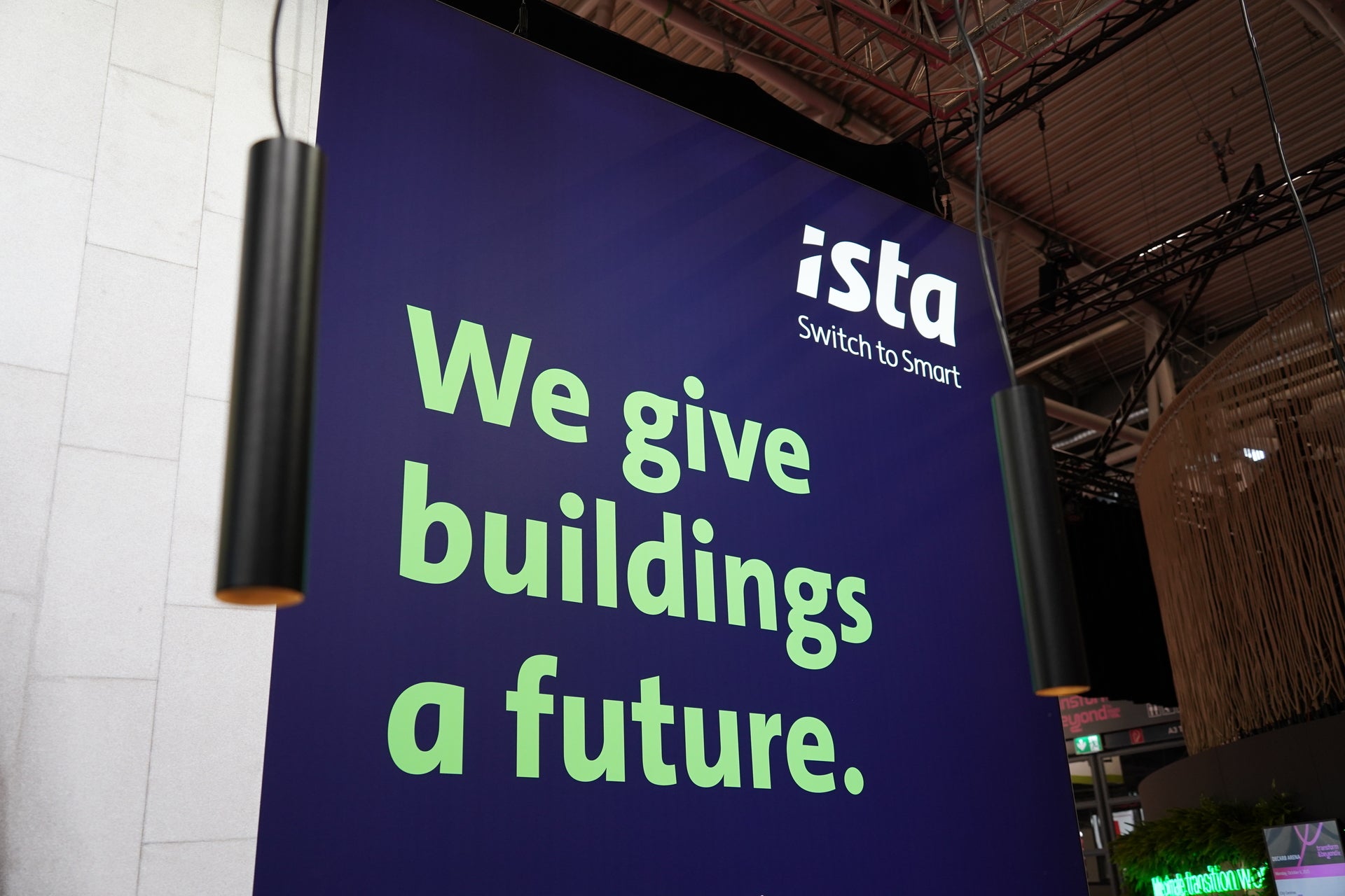 Großes Banner mit dem ista-Logo und dem Slogan „We give buildings a future.“ auf einer Messewand, umgeben von modernem Messedesign und Beleuchtung.