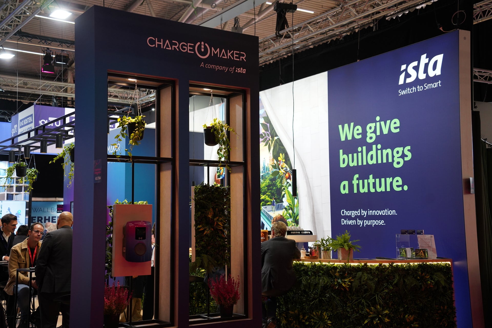 Messestand von ista und ChargeMaker mit grüner Pflanzenwand, Sitzbereich und dem Slogan „We give buildings a future.“ im Hintergrund, beleuchtet in moderner Atmosphäre.
