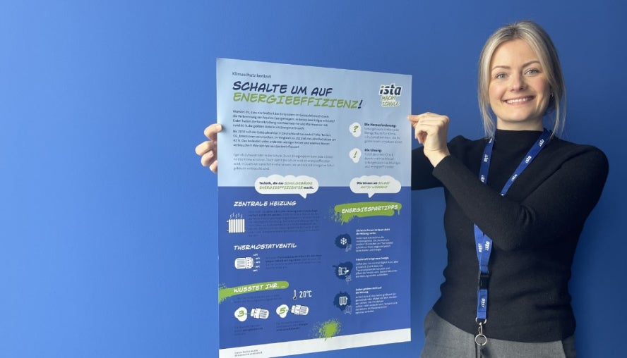 Auf dem Bild sieht man die ista Kollegin Maike Böcker. Sie steht vor eine blauen Wand und hält lächelnd ein Plakat zu den Projekt „ista macht Schule“ hoch. Sie hat blondes langes Haar, das zu einem Zopf gebunden ist. Außerdem trägt sie einen schwarzen Pullover und eine graue Hose. Um ihren Hals ist ein blauer ista Schlüsselband umgehängt.