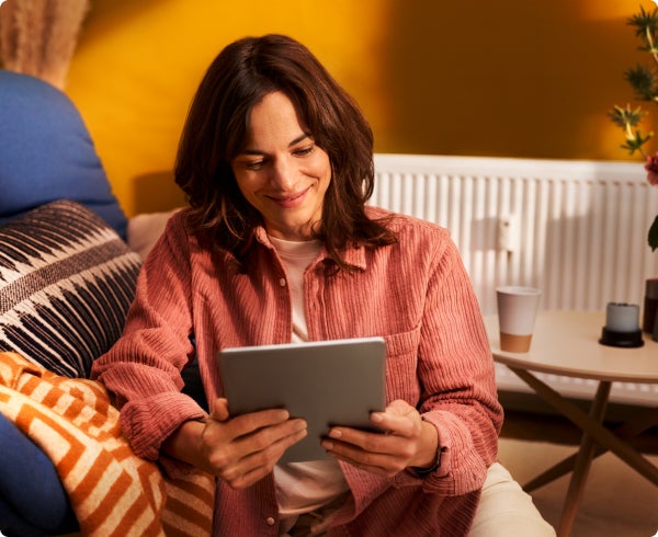 Eine Frau mit langen braunen Haaren, blickt Zufrieden auf ein silbernes Tablet in ihren Händen. 