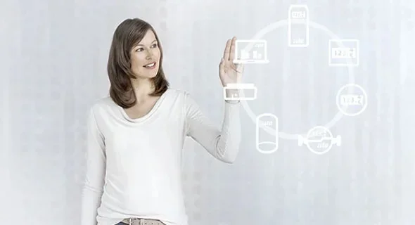 Eine Frau mit weißem Longsleeve betrachtet ein Hologramm welches einen Kreis mit mehreren verbundenen Geräten zeigt.