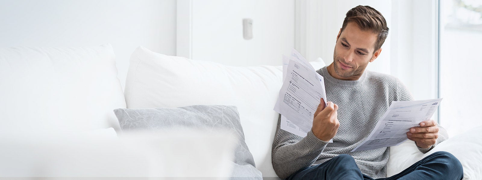 Ein Mann sitzt auf einer Couch. In den Händen hält er mehrere Blätter Papier. Es handelt sich um die Wasserabrechnung der ista. Sein Gesichtsausdruck ist dabei neutral.